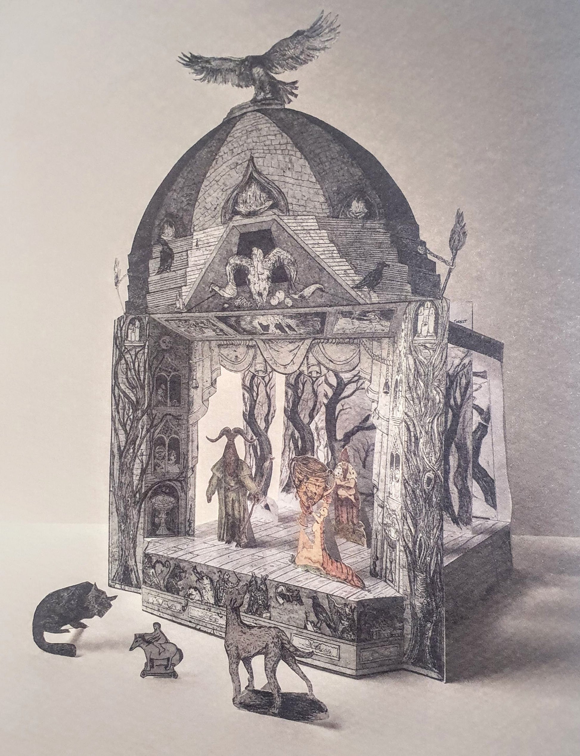 A three-dimensional paper toy theatre featuring a gothic-style magical show scene, with a bird perched on the roof, and various magical characters, perhaps sorcerers or witches, on the stage. Further small figures and animals stand in the foreground in front of the theatre.