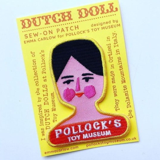 A sew-on patch with a illustration of a Dutch doll's head and the text 'POLLOCK'S TOY MUSEUM'. It is presented on a card backing.