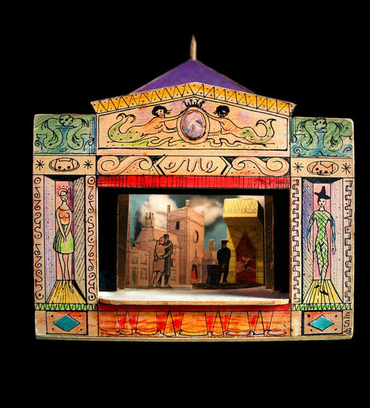 A photograph of a toy theatre, featuring a couple embracing in front of a building on the stage.