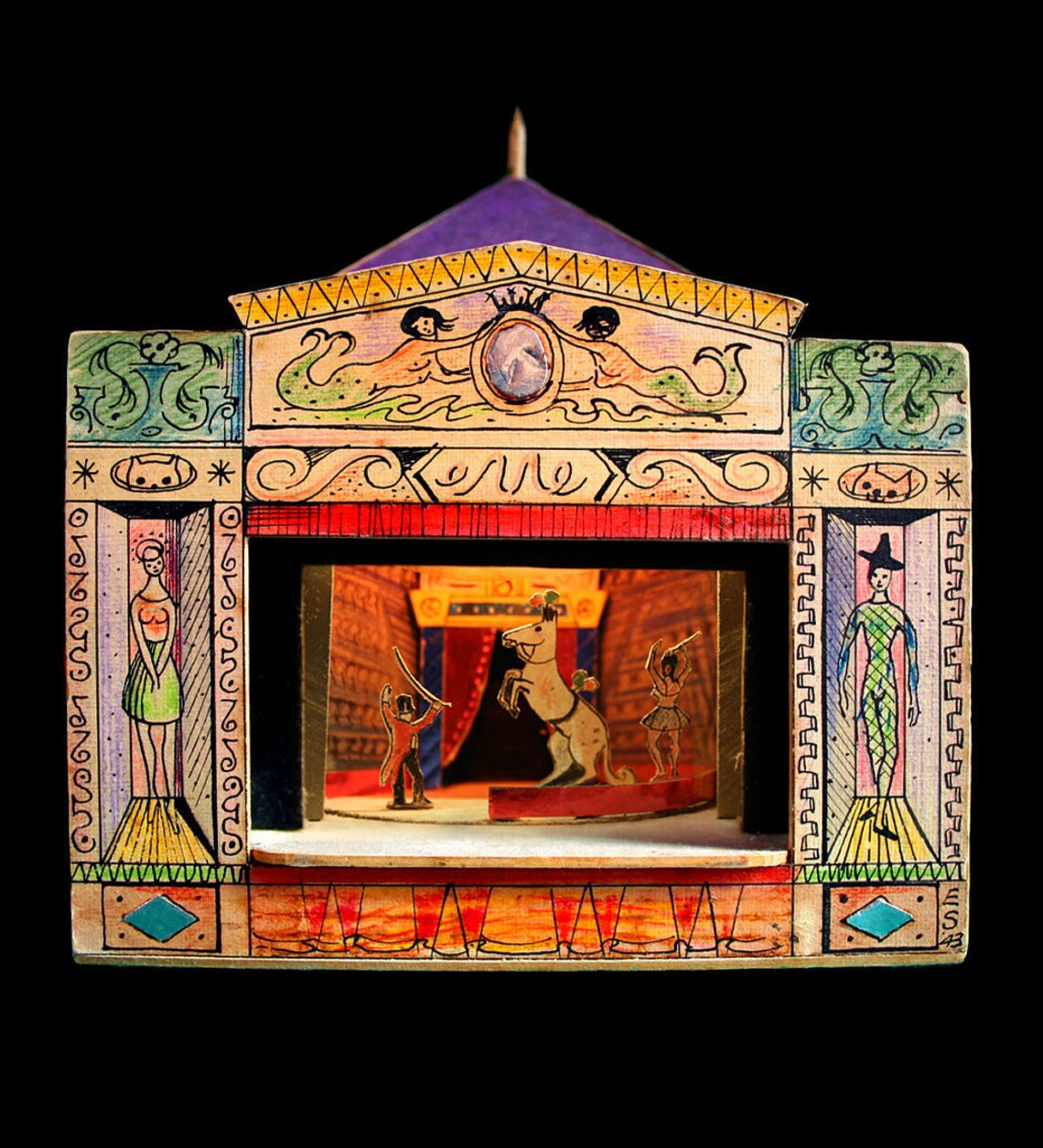 A photograph of a toy theatre, with a circus scene on stage, including a man and a lady performing with a pom-pom wearing horse.